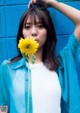 A woman holding a yellow flower in front of a blue wall.