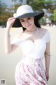 A woman in a white dress and a black hat on the beach.