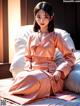 A woman in a pink kimono sitting on a bed.