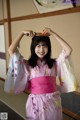 A woman in a pink kimono holding an orange on her head.