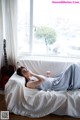 A woman laying on a white couch in front of a window.