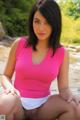 A woman in a pink top and white skirt sitting on a rock.